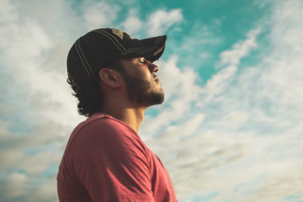 Man with cap, eyes closed cloudy sky background