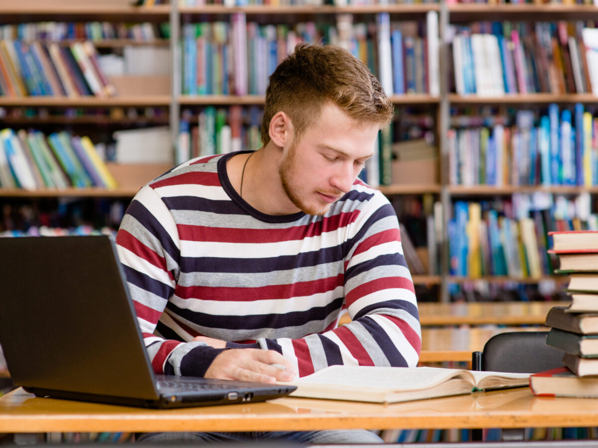 Student in library with laptop studying books